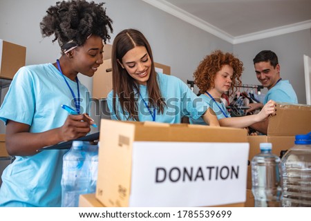 Group of multiethnic volunteers putting food and drinks into paper box for charity. Group of people working in charitable foundation. Happy volunteer looking at donation box on a sunny day.