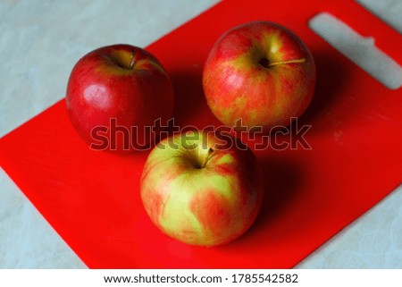 Three red apples on a red Board on the table