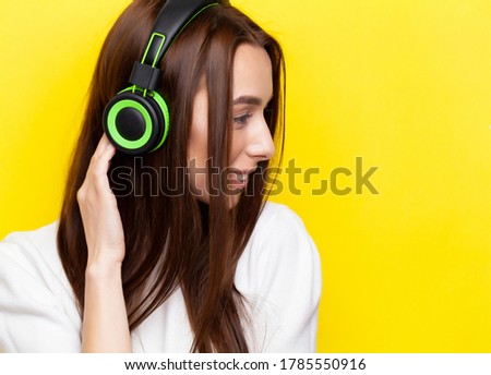 Beautiful young woman in headphones on yellow background