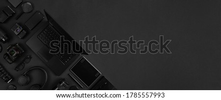Top view of of photography gear and laptop geometricaly arranged on abstract black background. Minimal tech layout dark desk flat lay.