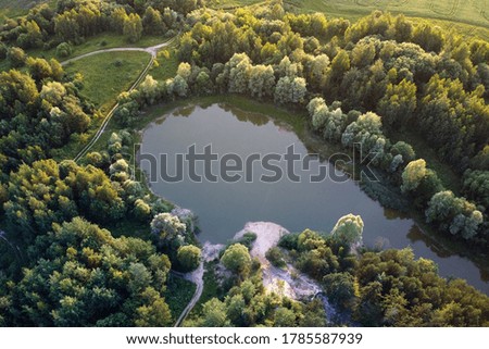 Aerial view - small lake in a forest and field, sunset light. European nature.