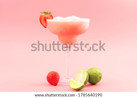 Mixed cocktails, party punch smoothies and frozen summer drinks concept with strawberry mojito or daiquiri in margarita glasses, strawberries and limes isolated on pink background