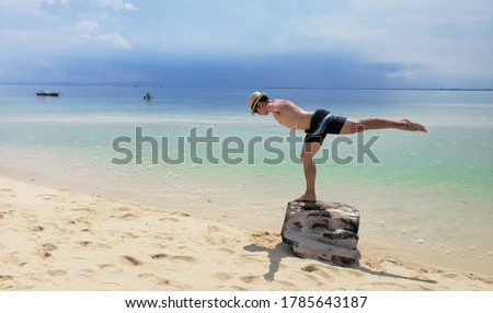 A guy doing balance pose on top of a rock on a beach sand 