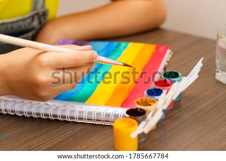 Young African American kid girl drawing or painting rainbow picture.