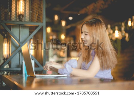 A happy woman is working with a laptop at a coffee shop in Thailand.