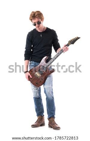 Young cool red hair rock guitarist holding electric guitar looking down. Full body length isolated on white background. 