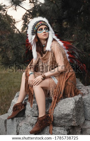 beautiful Indian woman in roach, dress with fringes and makeup on her face, is sitting on the rock