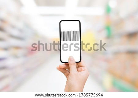 Shopping and Retail Concept  Hand holding smartphone that showing barcode on white screen and blurry image of supermarket in background.
