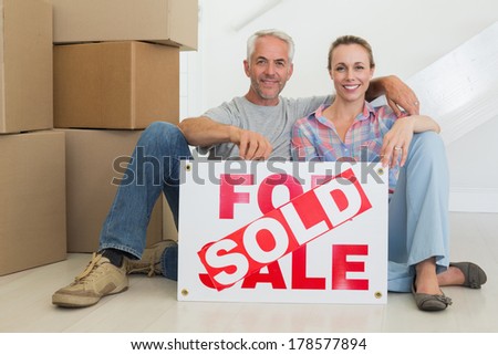 Happy couple sitting on floor with sold sign in their new home