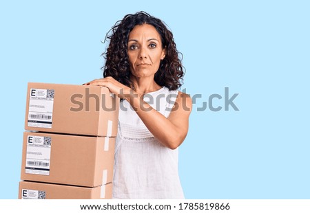 Middle age beautiful woman holding delivery package thinking attitude and sober expression looking self confident 