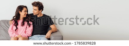Panoramic shot of man embracing beautiful smiling girlfriend on couch on grey background