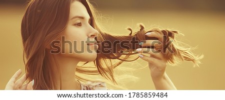 young brunette in summer with long hair in a field, happy person health beauty posing at sunset