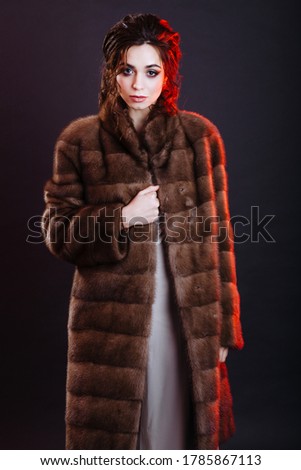Gorgeous fashion model in a brown fur mink coat with professional make-up and hairstyle posing indoor on a black background in studio. Image for fur boutique salon.
Concept of luxury fur outwear