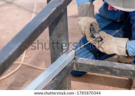 Man welds a metal with a welding machine, profession of welder. Arc welding of a steel in construction site. Industry worker welding iron pieces at work.