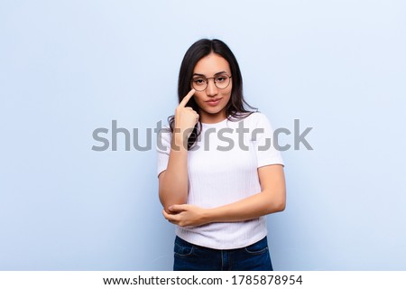 young latin pretty woman keeping an eye on you, not trusting, watching and staying alert and vigilant against flat wall Royalty-Free Stock Photo #1785878954