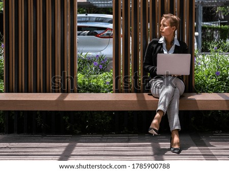 Business woman sitting on bench with laptop on lap stock photo
