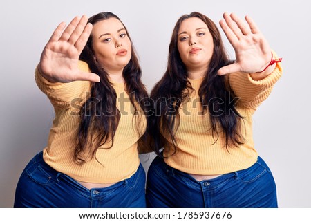 Young plus size twins wearing casual clothes doing frame using hands palms and fingers, camera perspective 