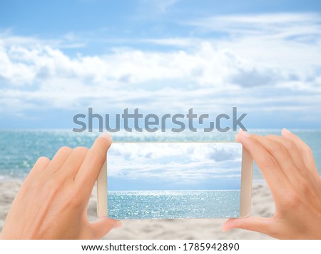 Hand woman Taking photo by smart phone with blue sea view on tuchscreen and blur image of sea and sky. for travel summer holidays at sea.