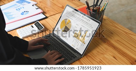 Cropped image of Businesspeople is using a computer laptop with graphic charts on screen at the wooden desk.