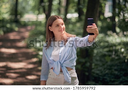 A young woman walks in the park in the summer and takes a selfie.