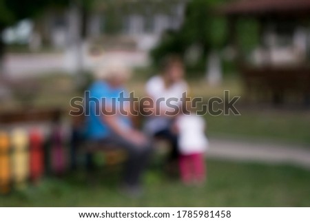 Blurred defocused family with little kid in the park. Playing on the grass at the playground. Generation of unrecognisable grandmother, mother and child getting closer. Togetherness concept.