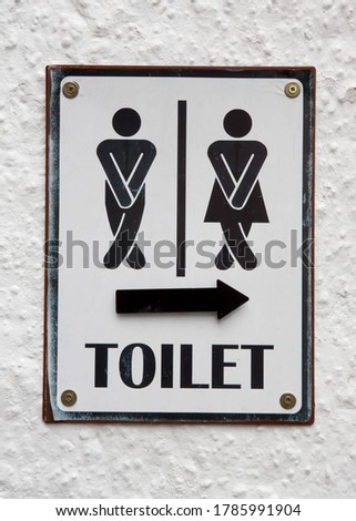 Sign showing a man and a woman crossing their legs needing to use a public toilet with an arrow pointing the way.
