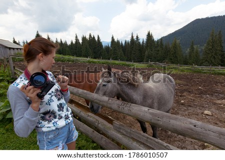 girl on a ranch in the mountains photographs a horse