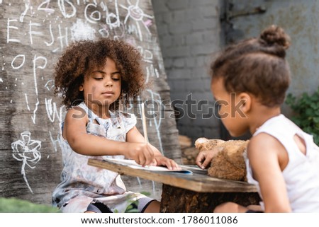 selective focus of poor african american kid writing in notebook near brother outside