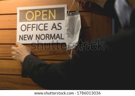 Business owner wears masks and hand is holding mask to label for open office. The concept is opening office after the COVID-19 situation, follows the new normal life. select tive focus