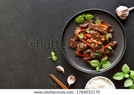Thai beef stir-fry with pepper and basil on plate on a dark stone background with copy space. Top view, flat lay Royalty-Free Stock Photo #1786032170