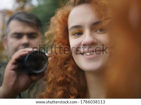 Young attractive model woman and man photographer reflected in the mirror. redhead curly female with smiley face