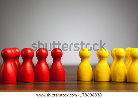 Opposition or confrontation concept with two red and yellow groups of toy pawn figures.