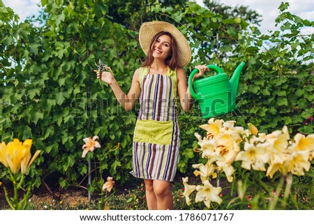 Woman watering flowers with watering can and cutting with pruner in garden. Gardener taking care of lilies.