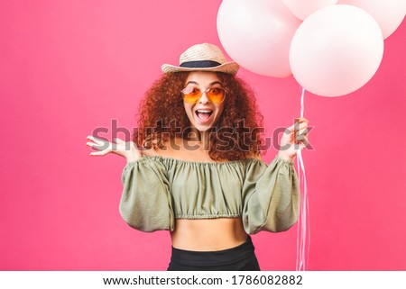 Happy holiday! Happy young curly smiling woman with balloons isolated over pink background. Valentines day or womans day.
