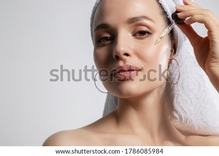Closeup studio portrait with young woman in bath towel on head isolated on copy space applying oil serum from pipette. Natural organic cosmetic product for facial skincare and skin regeneration