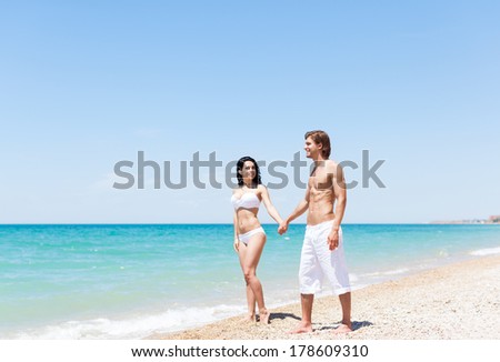Couple walking on beach, love hold hands. Young happy man and woman walk sea shore smiling romantic looking each other, summer ocean vacation holiday blue sky