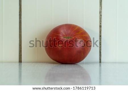Red tomato with gray spot and yellow stripes reflex in light table. Organic vegetables is good for healthy diet, because contains a lot of vitamins and minerals. Horizontal picture, copy space.
