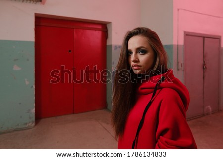 A beautiful girl of 20-25 years old in a red sweatshirt posing in an underground room. Portrait of a beautiful caucasian girl.