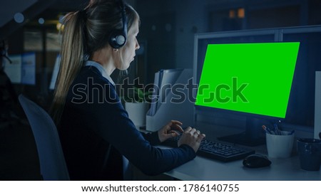 Working Late at Night in the Office: Handsome Businesswoman with Headphones Using Desktop Compute With Green Mock-up Screen. Call Center Worker, Financial Manager, Emergency Service Worker.