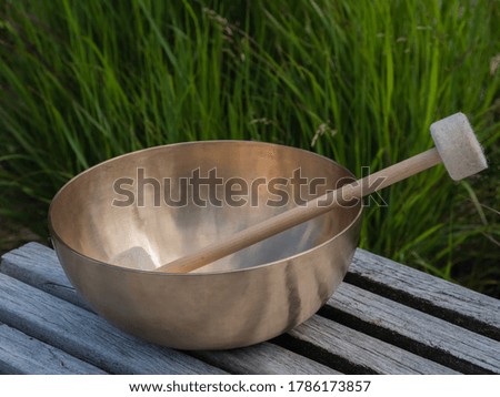 Singing bowl with mallets on a bench in front of green grasses

