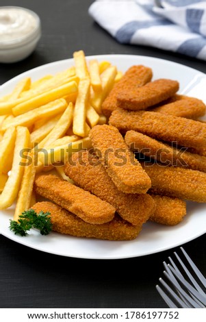 Homemade Fish Sticks and Fries with Tartar Sauce on a black background, side view.