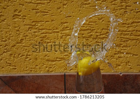 Lemon Falling into Glass Carafe caused O-Shaped Water Splash in front of Yellow Wall.