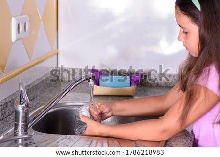 Girl rinsing a freshly washed glass in the kitchen sink. Helping with the housework. Selective focus.