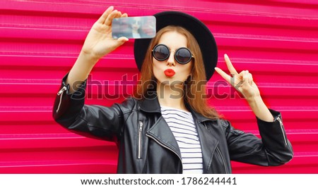 Attractive young woman taking selfie picture by phone blowing red lips sending sweet air kiss over colorful pink background