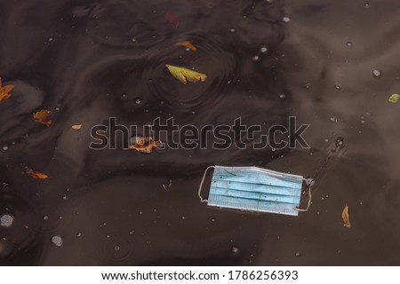Health care and protection from virus concept, Light blue surgical face mask thrown away in water after used, Waste procedure or medical mask in canal of Amsterdam, Netherlands. Royalty-Free Stock Photo #1786256393