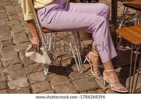 Street fashion details of elegant woman`s summer outfit: lilac trousers, white strap sandals, leather pouch handbag Royalty-Free Stock Photo #1786268396