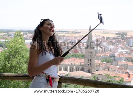 girl taking a picture with the mobile phone and a selfie stick with a panoramic view of a tourist city in the background. Burgos, gothic cathedral.