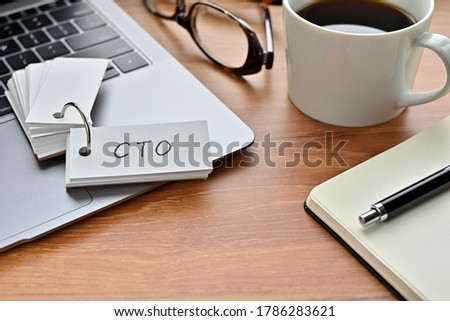 On a desk with a laptop, glasses, coffee, and a notebook, a vocabulary book was placed open There. The word CTO is there. It's an acronym that means chief technical officer.