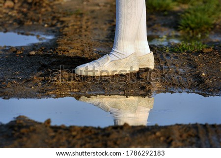 Girl's legs in white stockings and shoes in the mud after the rain. Mud, puddles and girl.