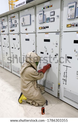 The electrician wear arc flash suit, electrical safety gloves and high voltage insulating boots to opening for switching-device track operation of circuit breaker panel Royalty-Free Stock Photo #1786303355